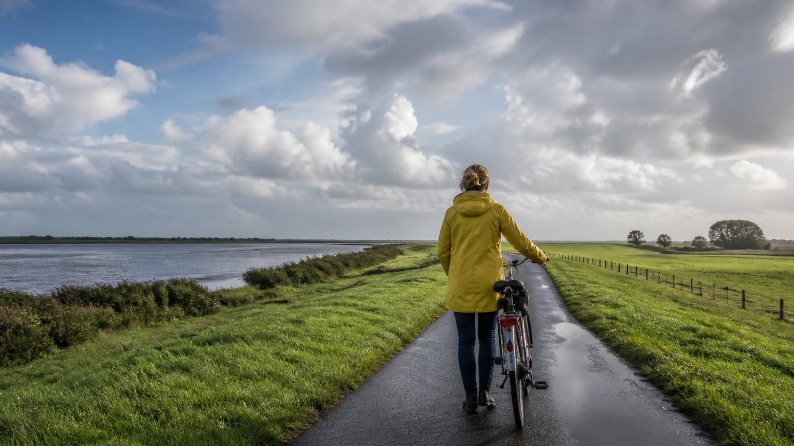 Een fietser rijdt voorbereid door wisselvallig weer op een Nederlandse dijkweg